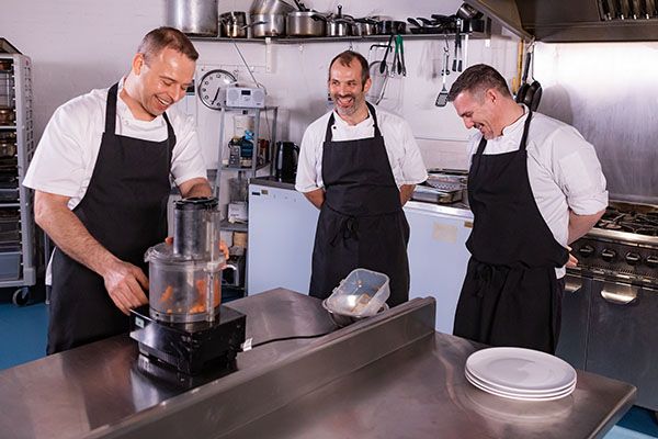 three chefs using a food processor in a resteraunt kitchen