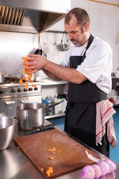 Chef in a restaurant kitchen dropping carrots into a saucepan