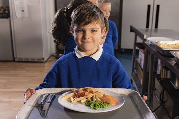 Young boy in school uniform holding out a diner tray, smiling